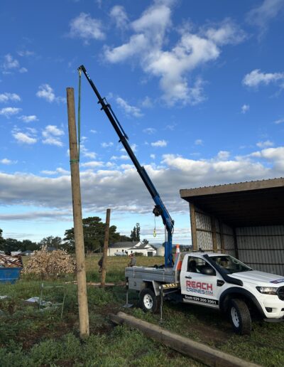 A timber pole is lifted for a shed installation on a rural property using a Reach Cranes mini crane.