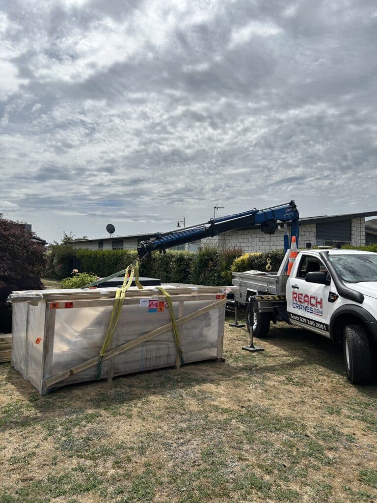 A crated shed positioned on a residential lawn after being delivered by Reach Cranes using a mini Hiab for precise placement.