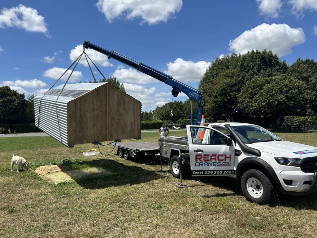 A Reach Cranes mini Hiab lifting a complete shed over a paddock in Cambridge, showcasing precise shed placement in rural conditions.