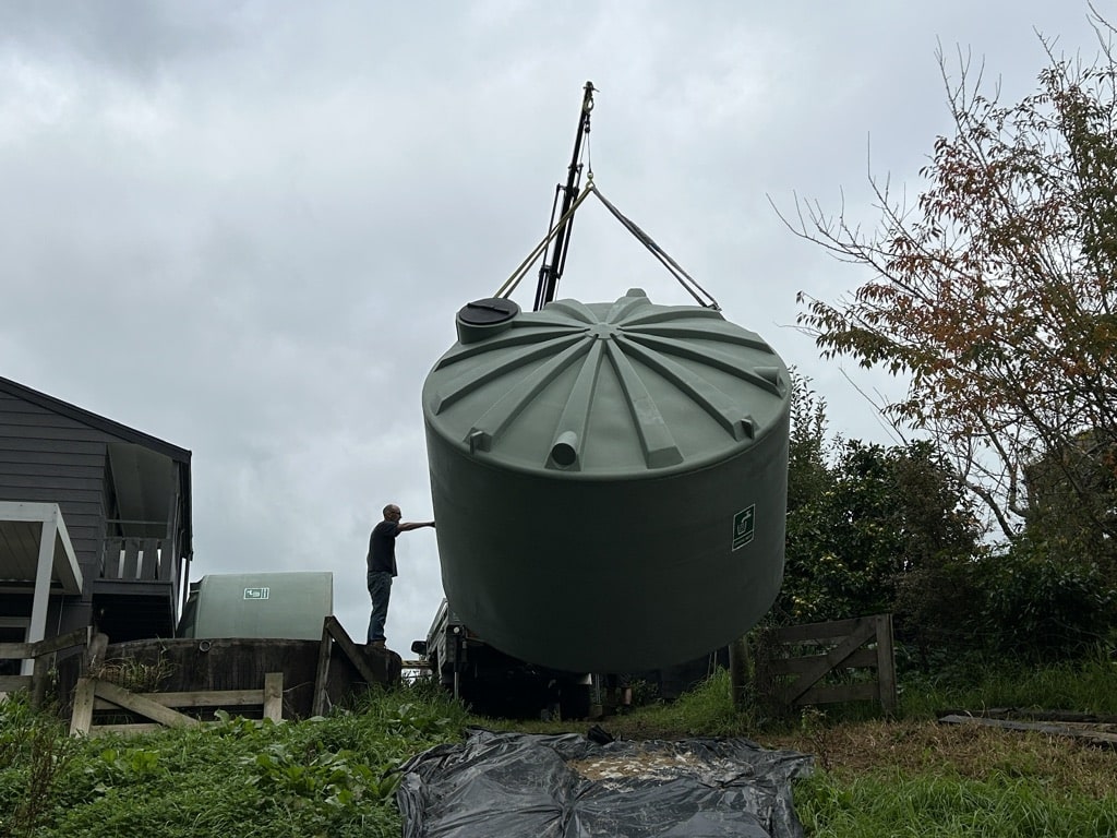 A large green water tank being lifted by a mini Hiab crane in Raglan, guided into place by a Reach Cranes operator.