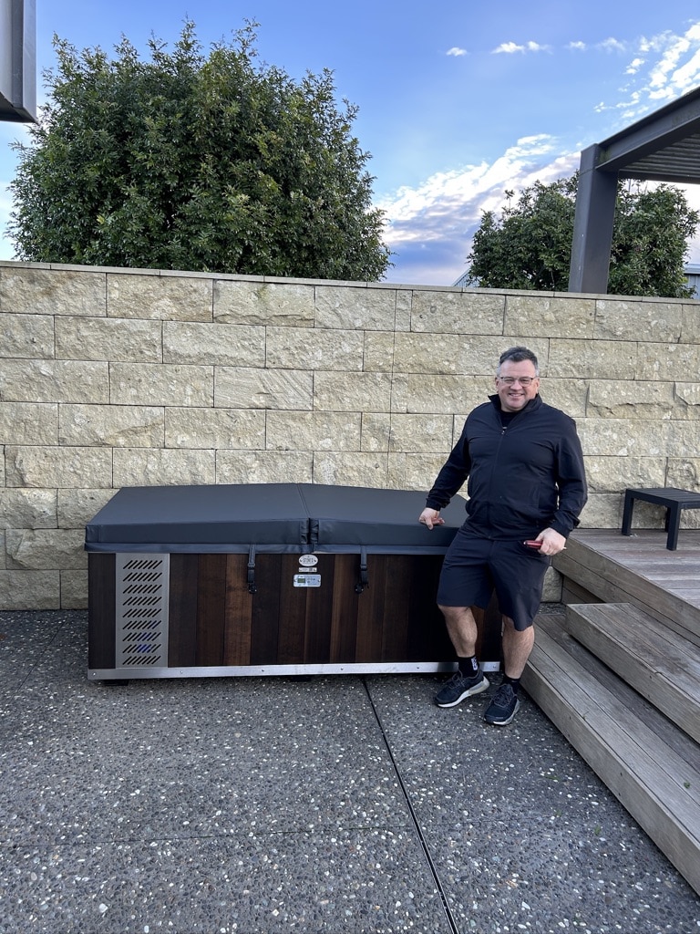 A customer standing beside a newly installed Stoked Stainless ice bath on a patio, delivered using Reach Cranes' mini Hiab in Hamilton