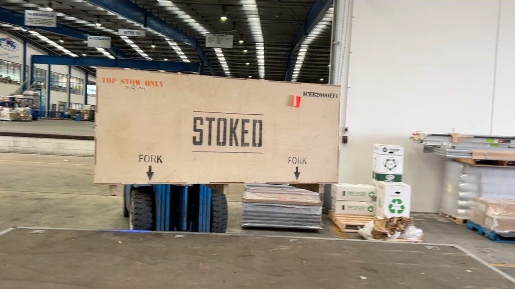 A large wooden Stoked Stainless crate on a forklift inside a warehouse, prepared for spa pool delivery with Reach Cranes' Hiab hire services.